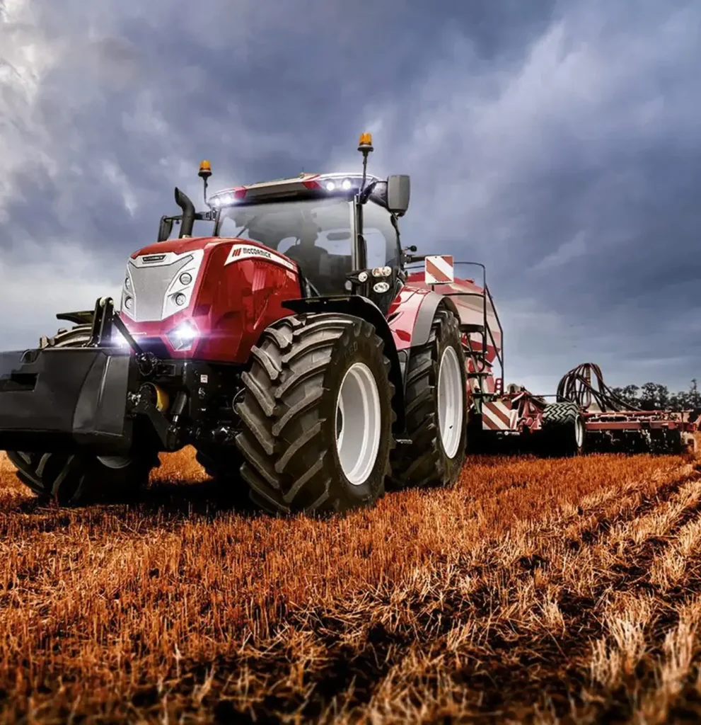 A red tractor driving through a green field under a clear blue sky.